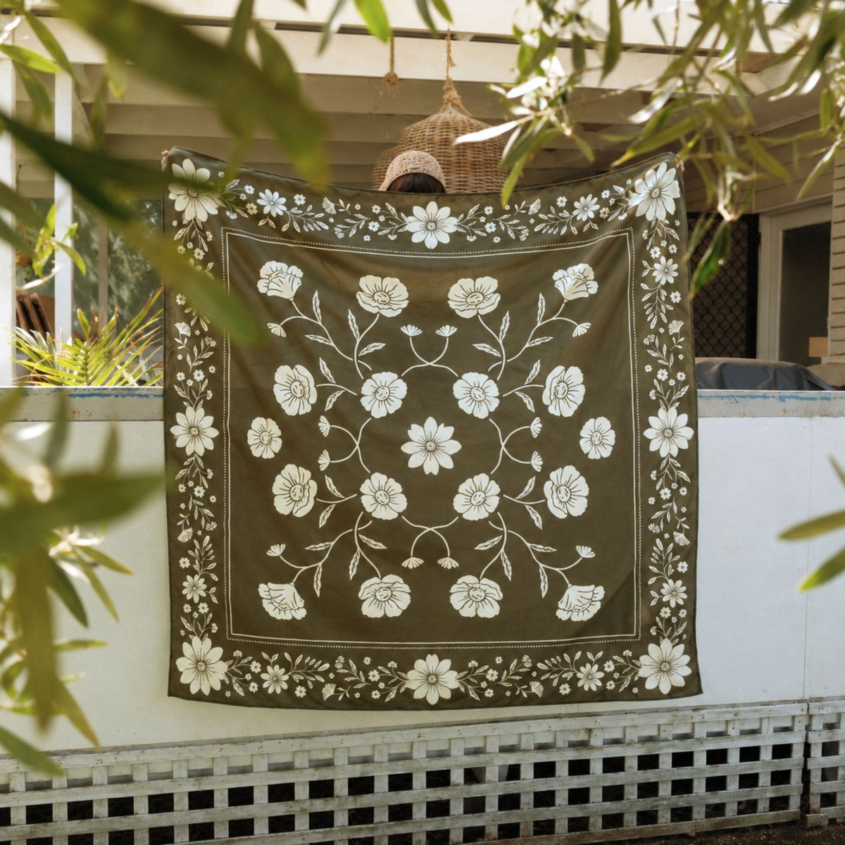 Eden sand free beach towel in XL, olive green floral bandana print, held up in a leafy garden