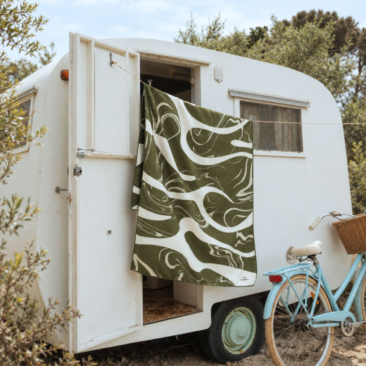 Liquid Dreams sand free beach towel in Large, green and cream marble swirl print, hung on a caravan, side view