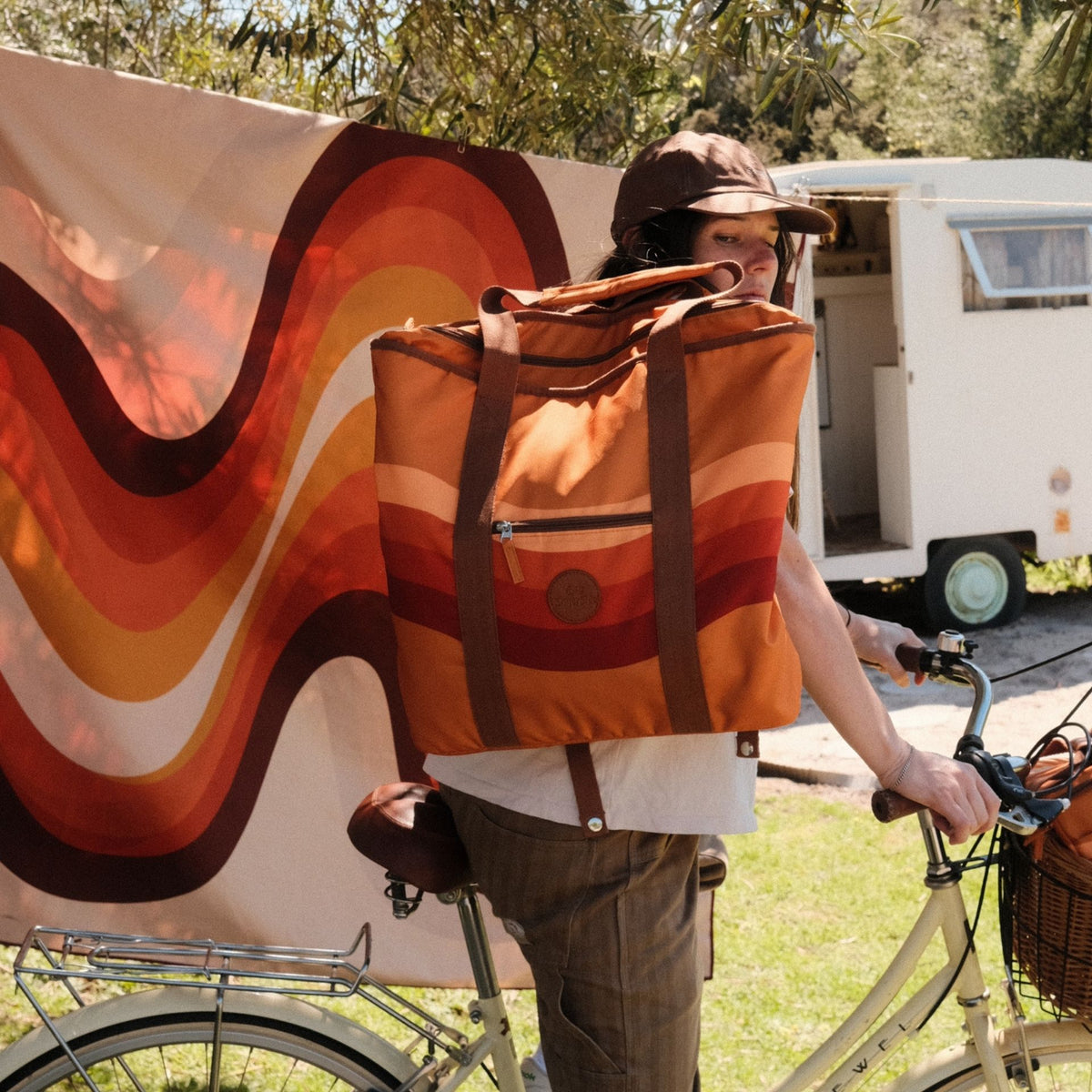 Stevie beach tote bag, orange retro 70s wave print, worn as a backpack by a bike and caravan