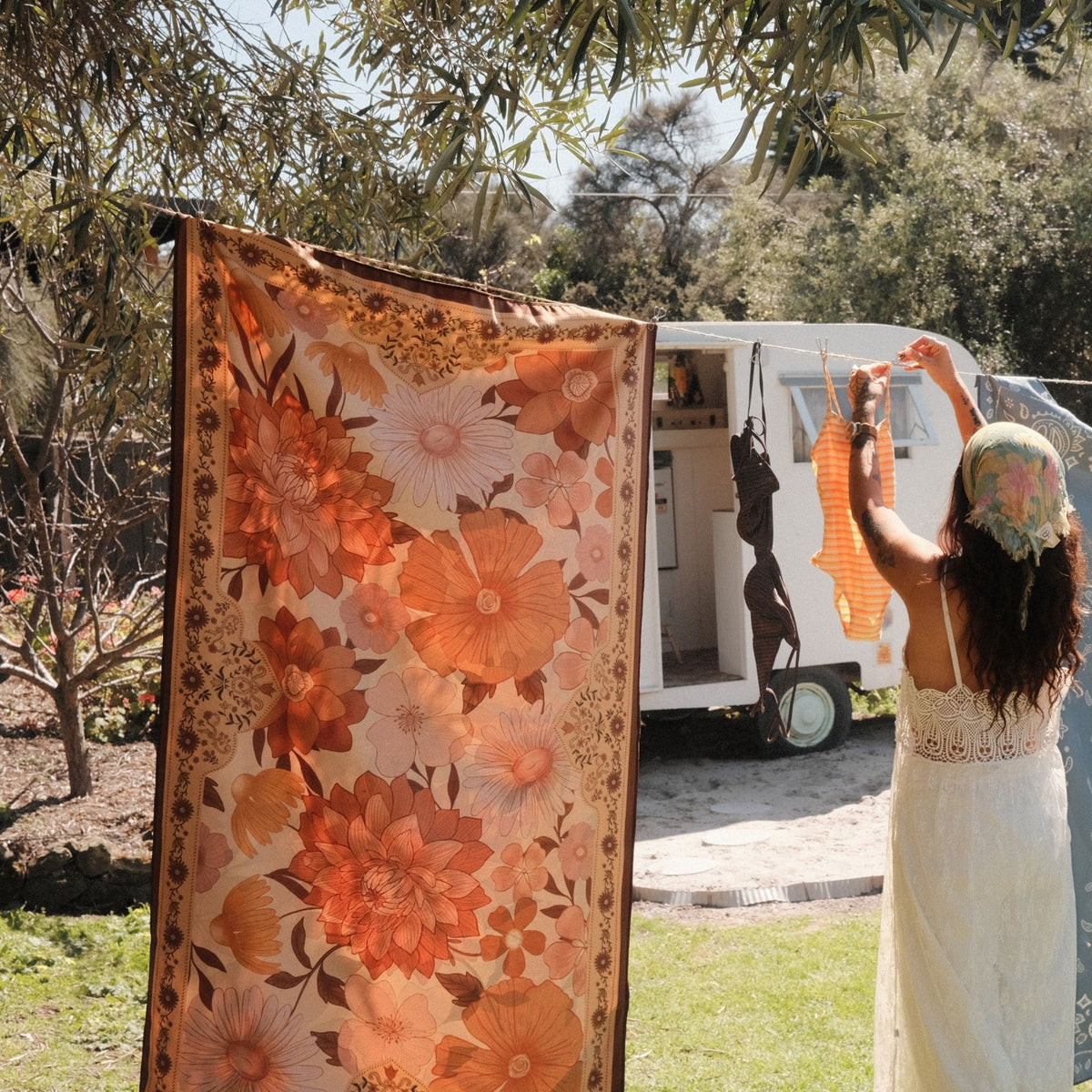 Summer Muse sand free beach towel in Large, peach retro 70s floral print, on a washing line by a caravan