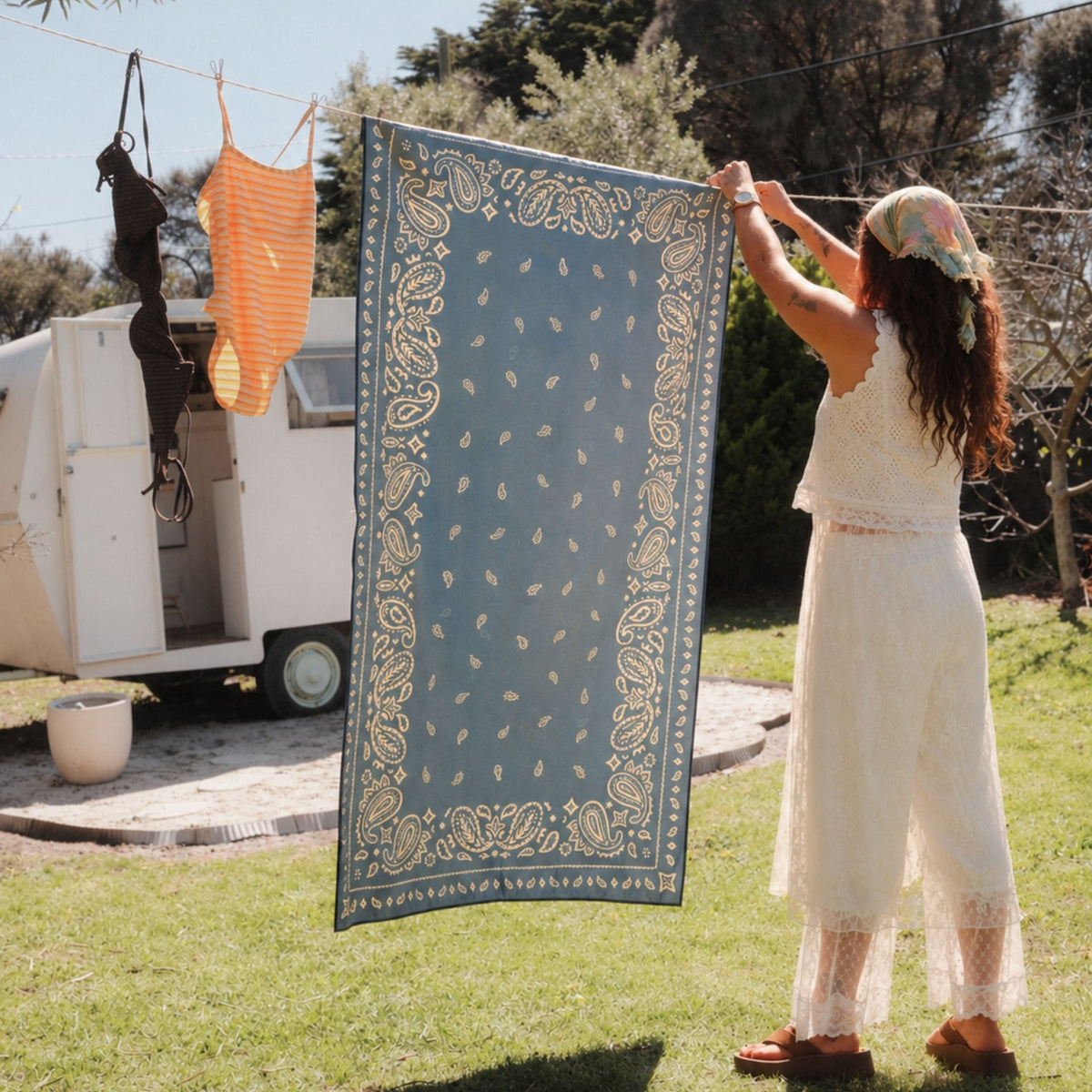 Venice sand free beach towel in Large, dusty blue paisley bandana print, on a washing line by a caravan