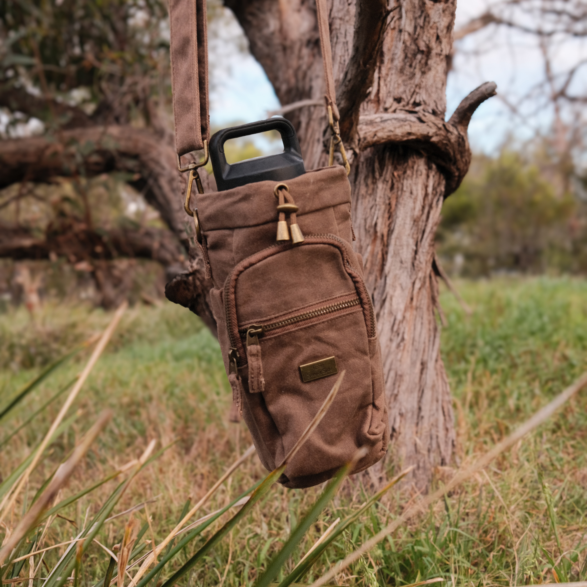 Brown waxed canvas bottle bag hanging on a tree branch
