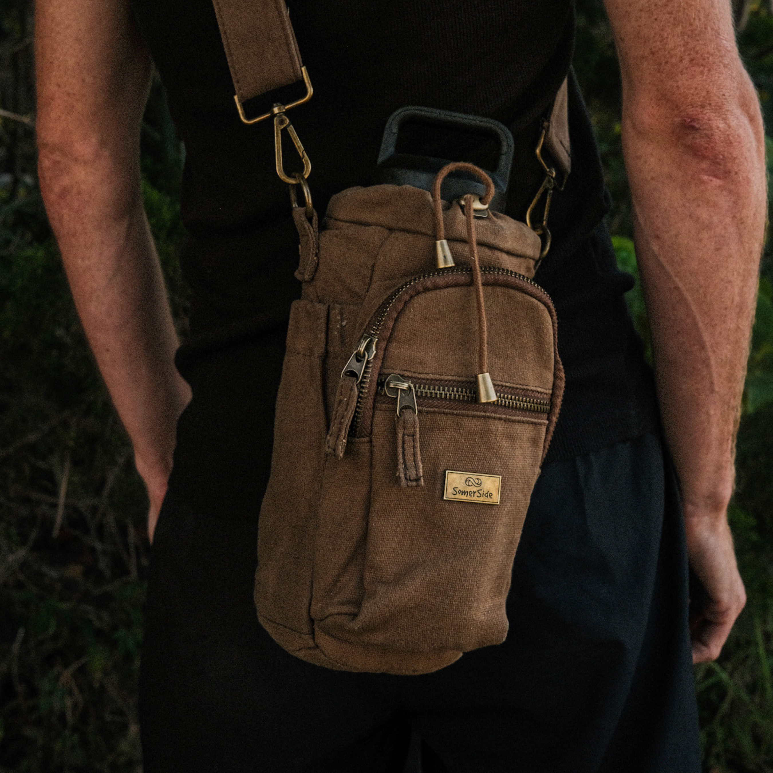 Brown waxed canvas bag with multiple zippers worn over a shoulder, set against a natural background
