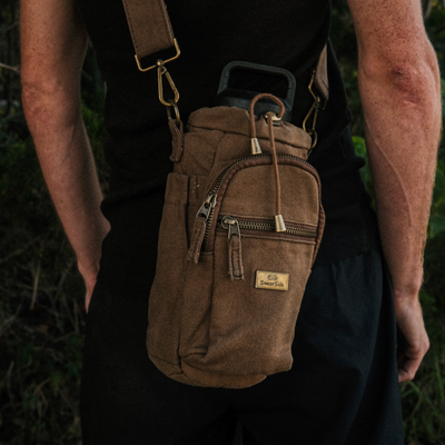 Brown waxed canvas bag with multiple zippers worn over a shoulder, set against a natural background