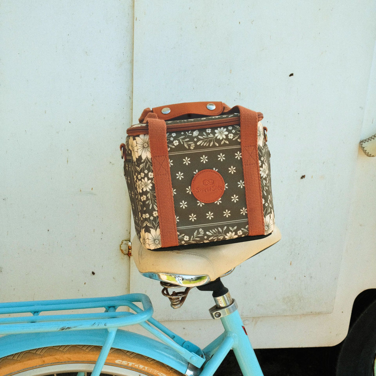 Eden mini insulated cooler bag, olive green floral bandana print, on a bike seat by a vintage caravan