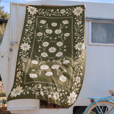 Eden sand free beach towel in Large, olive green floral bandana print, held up at a caravan