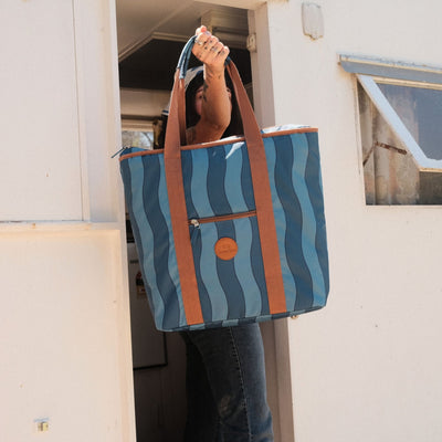 Jagger Tidal beach tote bag, two-tone blue wavy stripe, held up at a vintage caravan