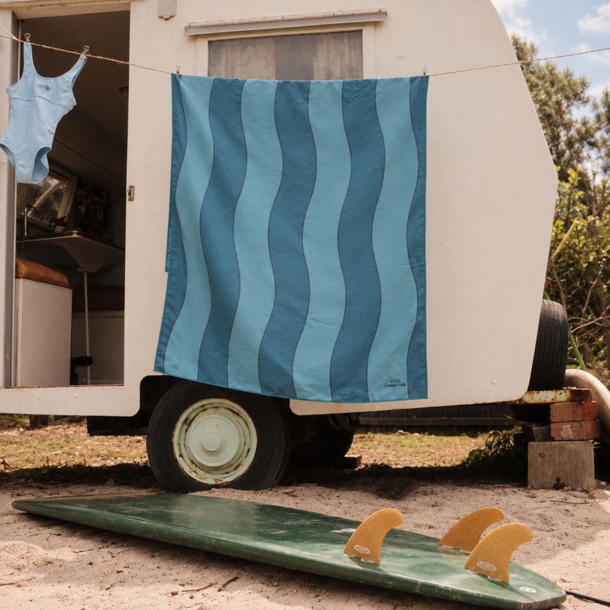 Jagger Tidal sand free beach towel in Large, two-tone blue wavy stripe, on a washing line at a caravan