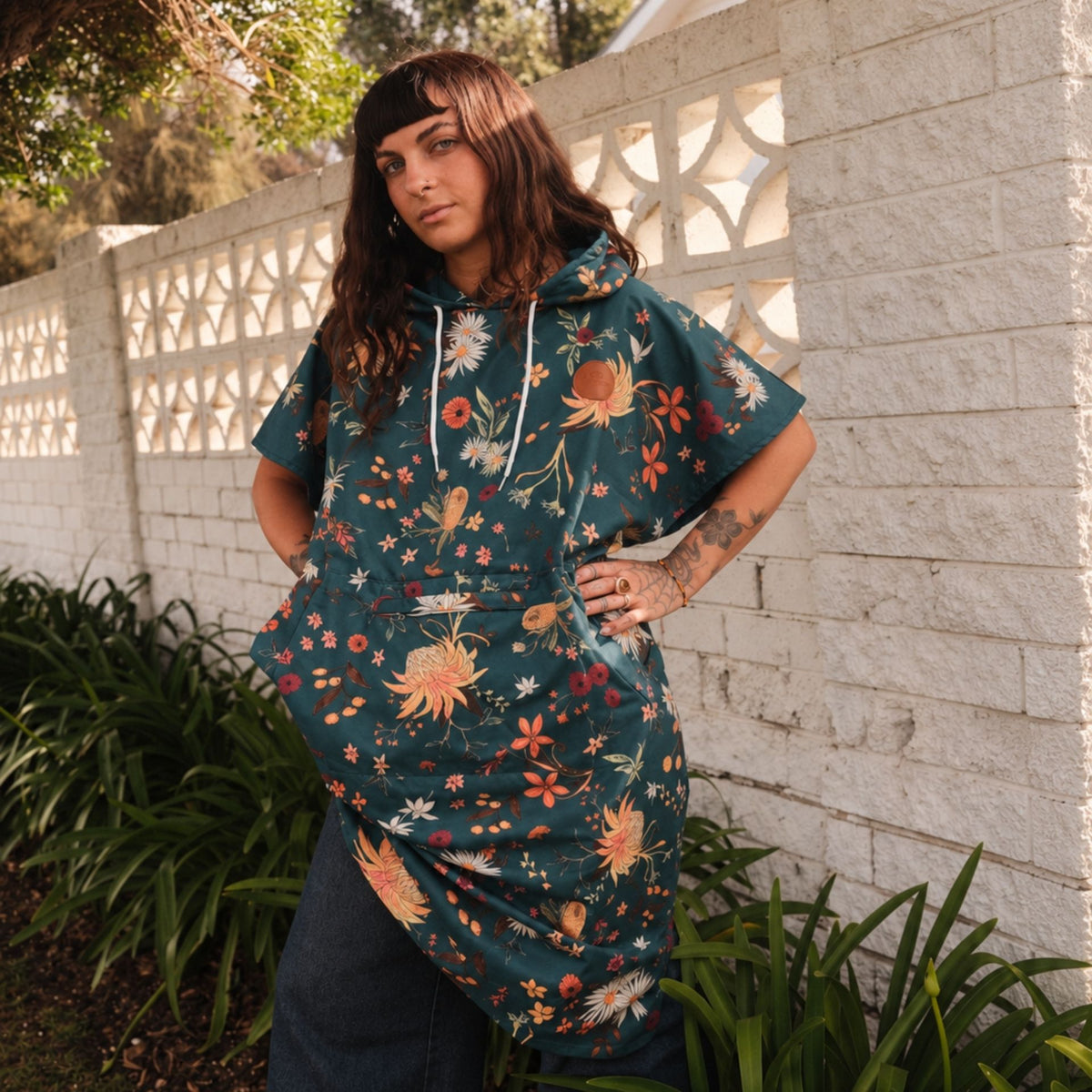 Native Botanical adult hooded towel poncho, dark green Australian wildflower print, by a breeze block wall