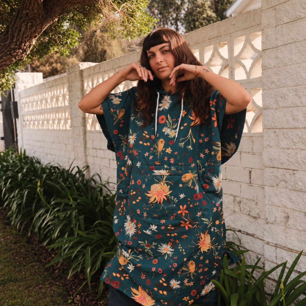Native Botanical adult hooded towel poncho, dark green Australian wildflower print, by a garden wall