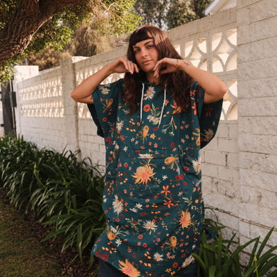 Native Botanical adult hooded towel poncho, dark green Australian wildflower print, by a garden wall