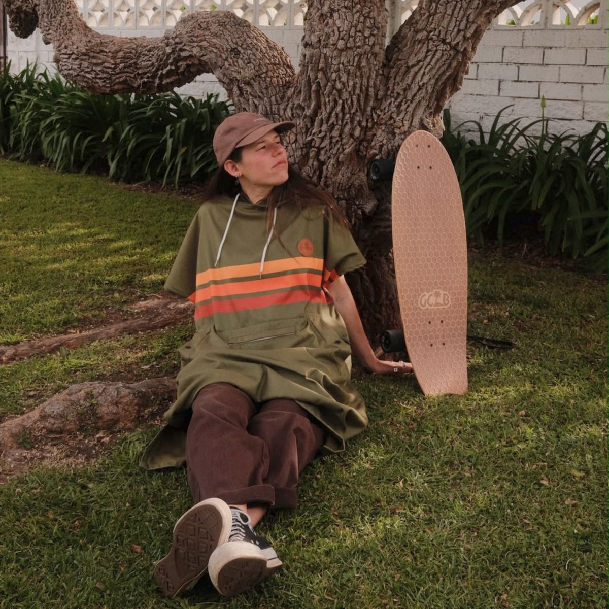 Stevie adult hooded towel poncho, olive green with retro orange stripes, sitting on the grass