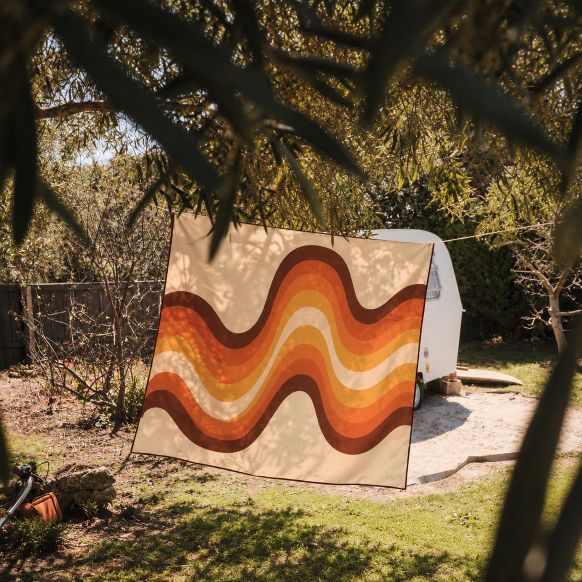 Stevie sand free beach towel in XL, orange retro 70s wave print, on a washing line by a caravan