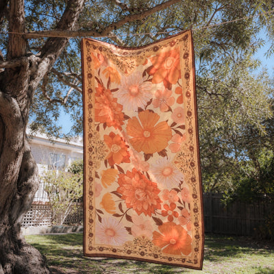 Summer Muse sand free beach towel in Large, peach retro 70s floral print, on a washing line under a tree