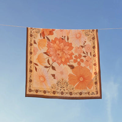 Summer Muse sand free beach towel in XL, peach retro 70s floral print, on a washing line against blue sky