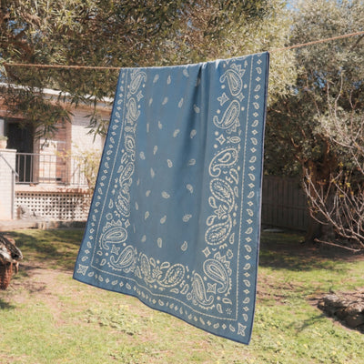 Venice sand free beach towel, dusty blue paisley bandana print, on a washing line in the garden